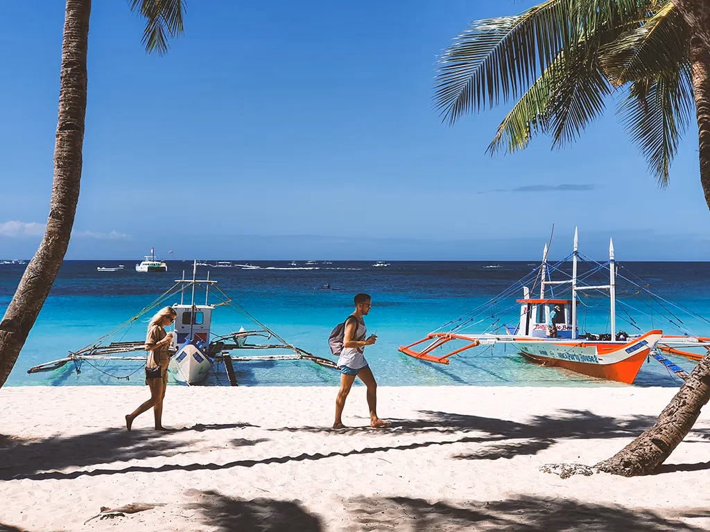 The iconic sunset at White Beach, Boracay, with soft sands, calm waves, and swaying palm silhouettes.